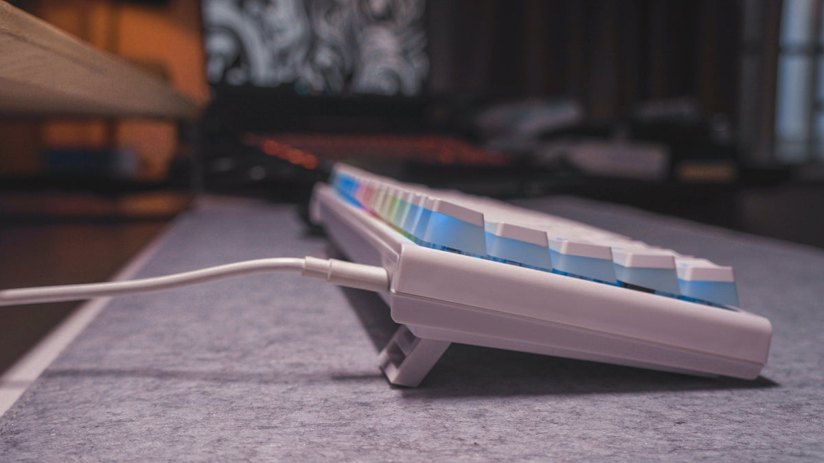 Low side view of a white mechanical keyboard with RGB light on a felt desk mat
