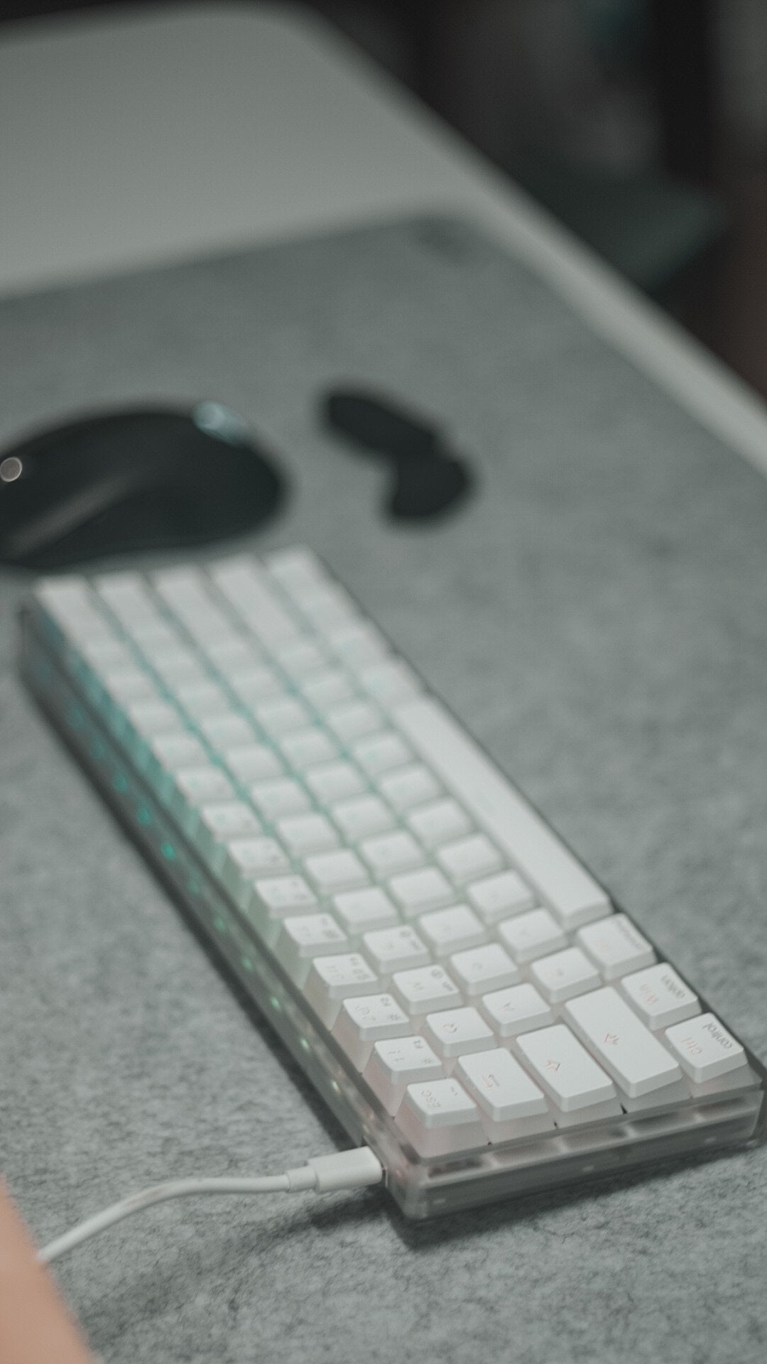 White mechanical keyboard and black mouse on a gray felt desk mat