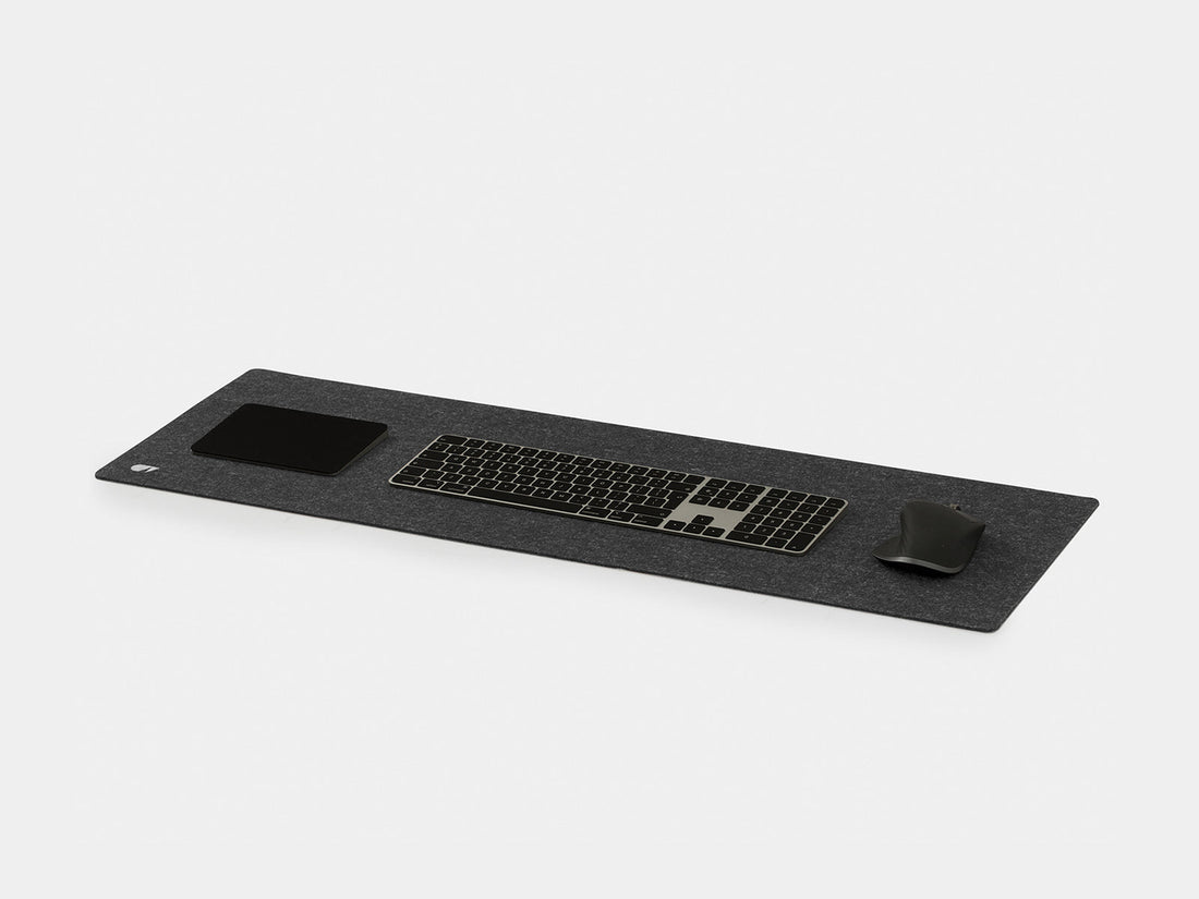 Anthracite felt desk mat at an angle with a keyboard, trackpad and mouse