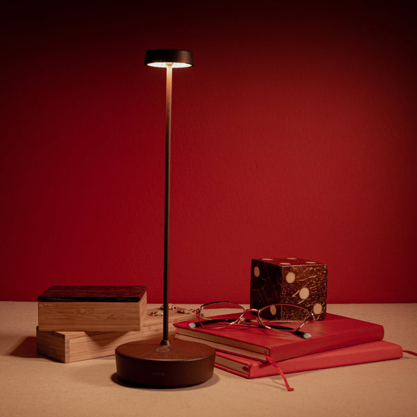A black Swap Pro lamp lit against a red wall beside books and a pair of glasses