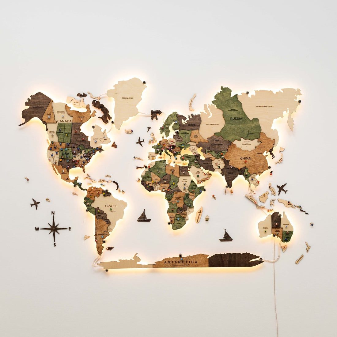 The full layered wooden world map on a wall with a warm backlight, a compass piece and a small wooden ship below it