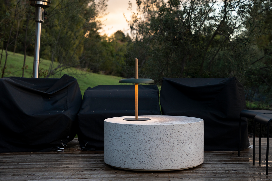 A green-shaded Nivel lamp on a white stone cylinder outdoors at dusk