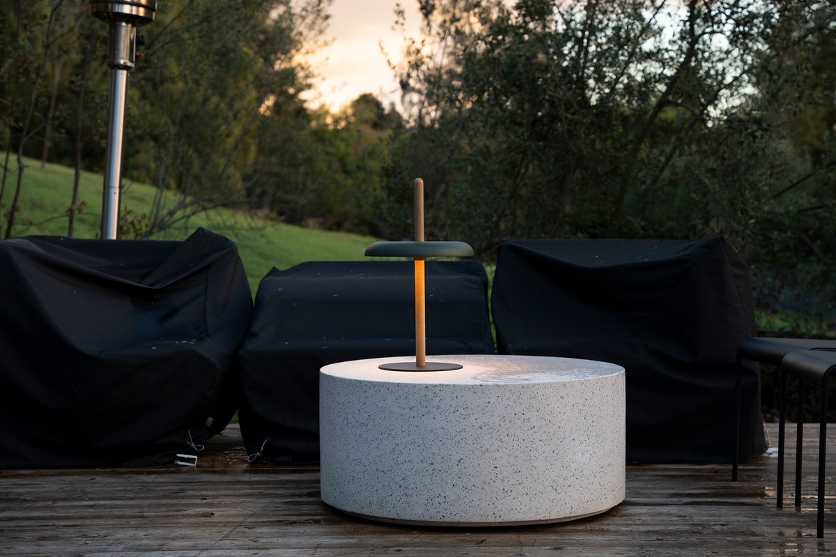 A green-shaded Nivel lamp on a white stone cylinder outdoors at dusk