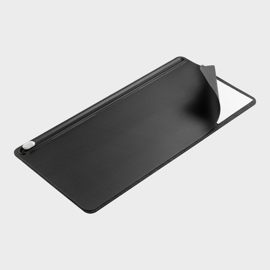 Black desk mat seen at an angle with one corner lifted to show a white sheet underneath, and a clip at the top edge