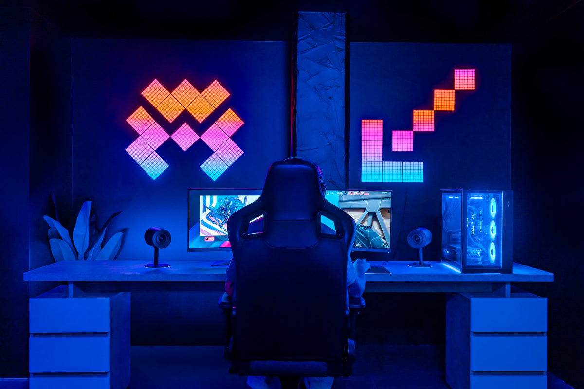 Two pixel-art light displays glowing in pink and cyan on the wall above a dark desk setup