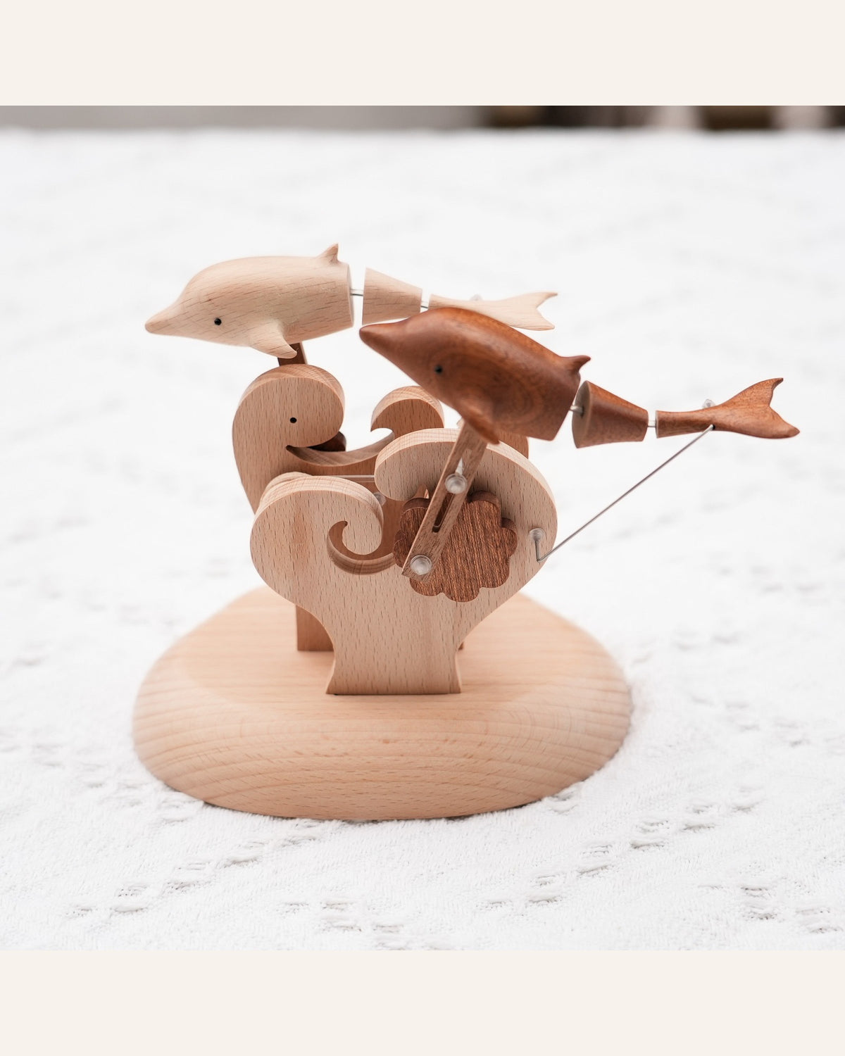 Pale and dark dolphins over carved waves on a pale wood base, front view on a white cloth.