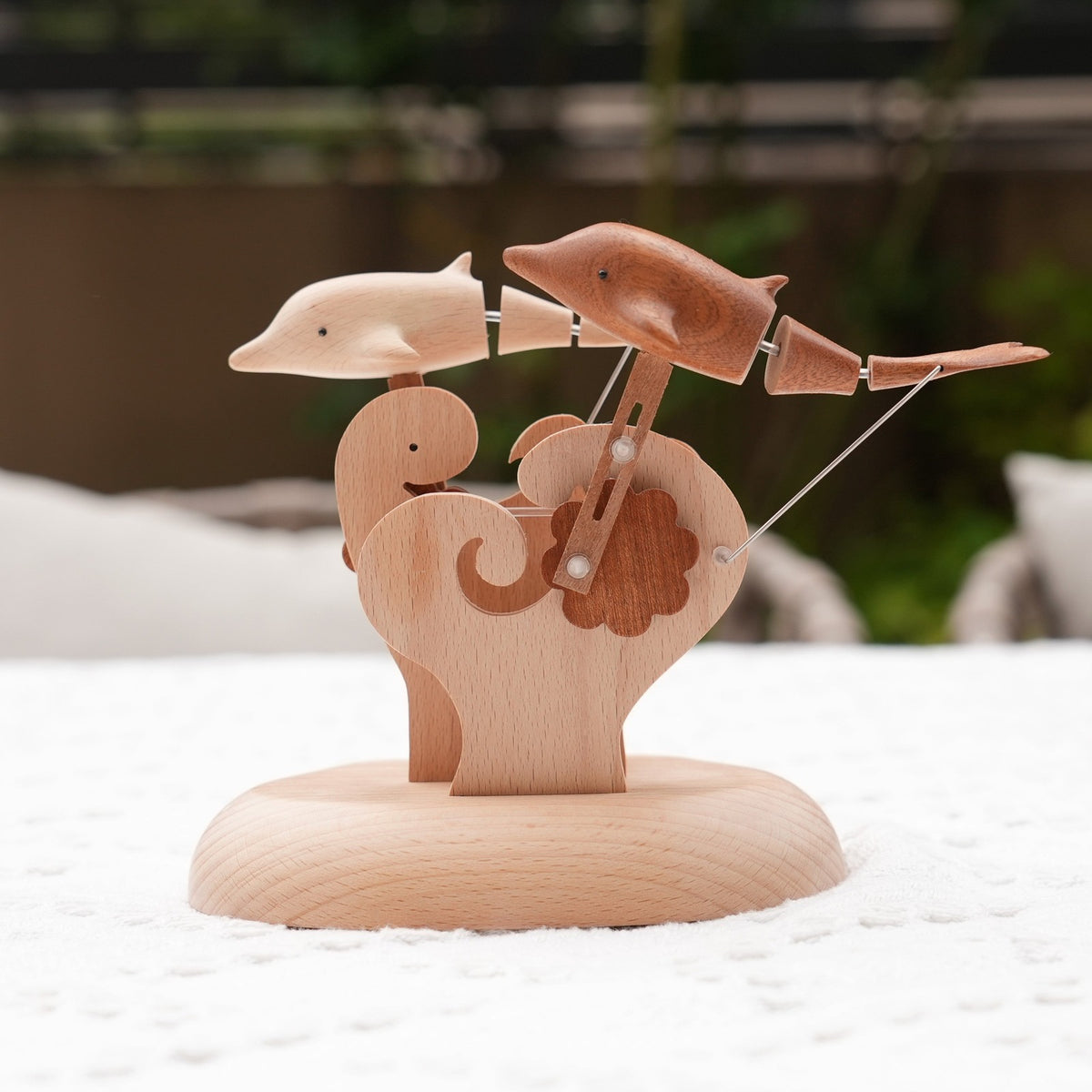 The pair of dolphins and the carved waves on a pale wood base, a blurred terrace behind.