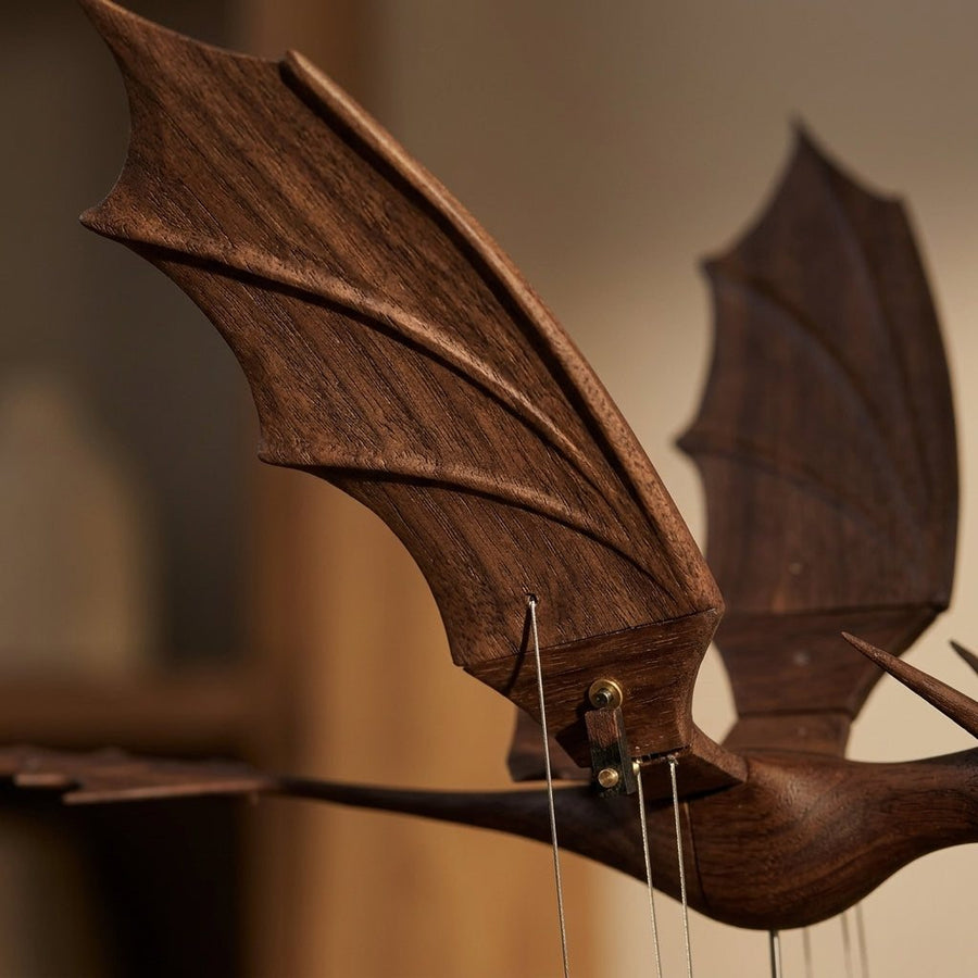 Close up of a dark ribbed dragon wing with thin wires meeting it, a second wing blurred behind.