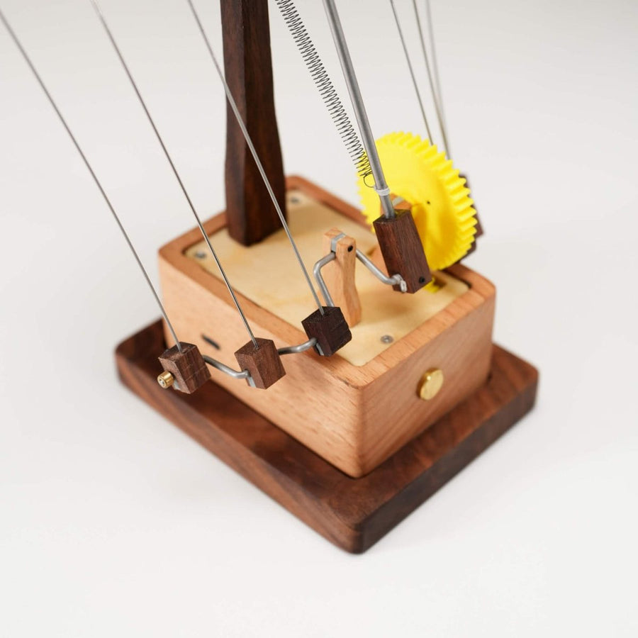 External gear base: a yellow gear wheel and cranks sit outside the wooden box, with thin wires rising to the manta ray.