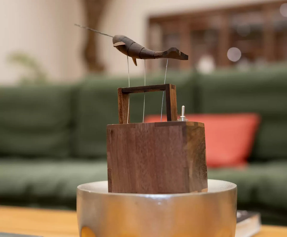 The narwhal automaton on a metal stand in a living room, a green sofa and red cushion blurred behind.