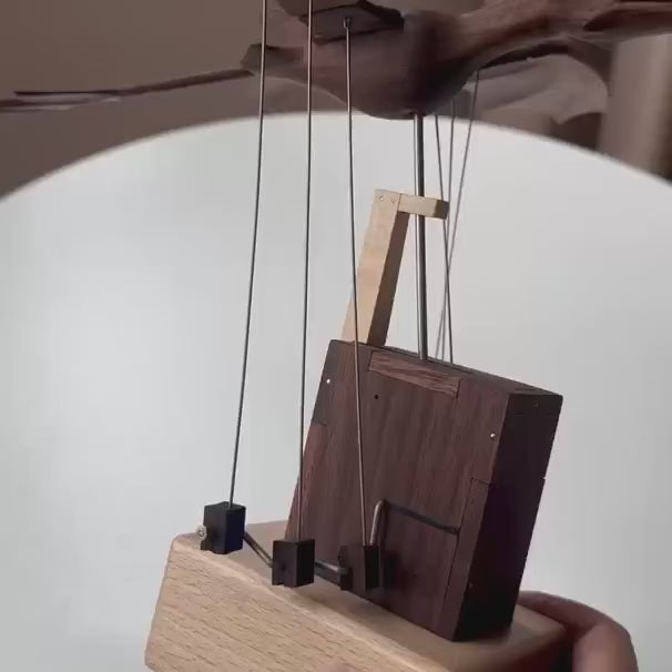 Close view of the dark wood tower and the thin wires that move the wings, a hand holding the light wood base.