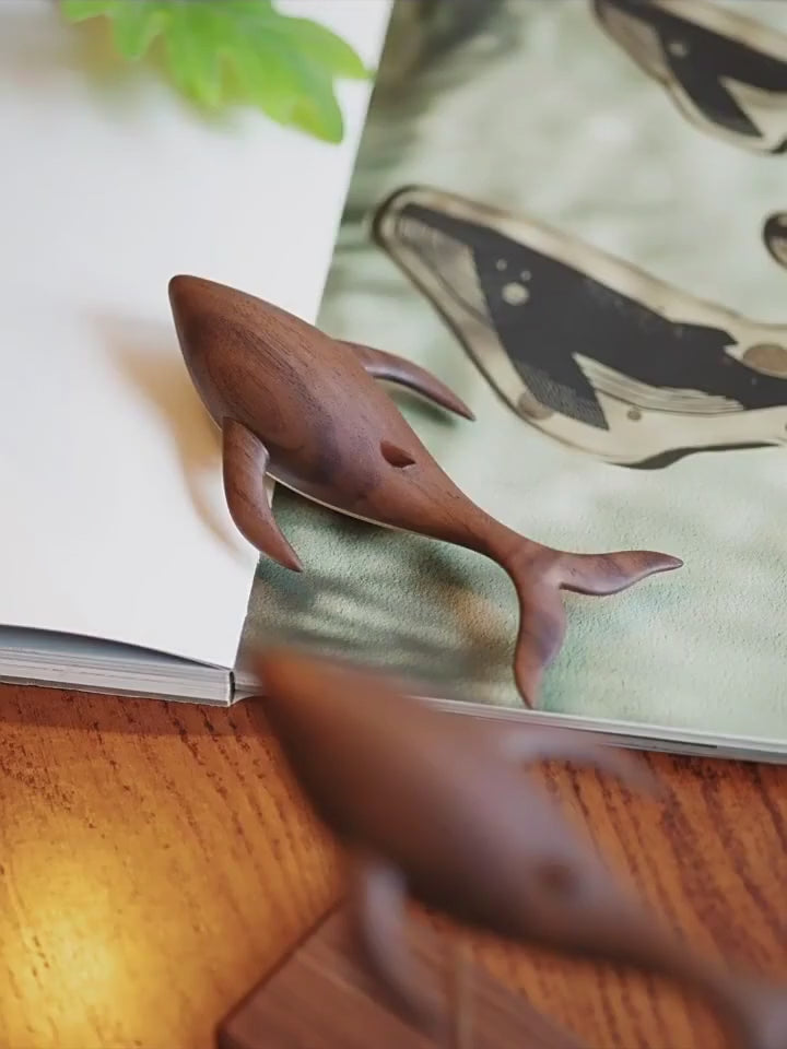 The walnut whale seen close above its maple base and on its brass rod, plants and a whale print around it.