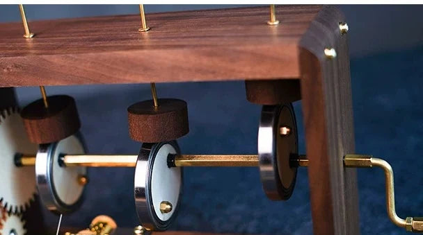 Close view inside the walnut frame: the gear wheel, three cams on a brass shaft and the rods they lift.