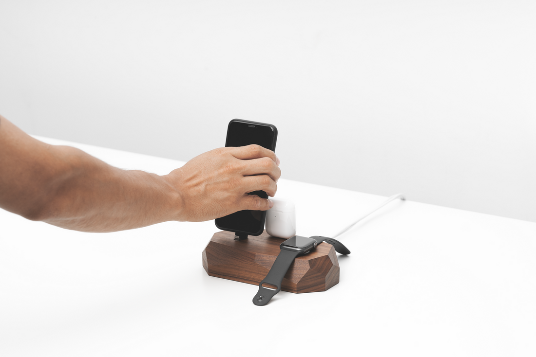 Hand lifting a phone from the walnut dock on a white desk