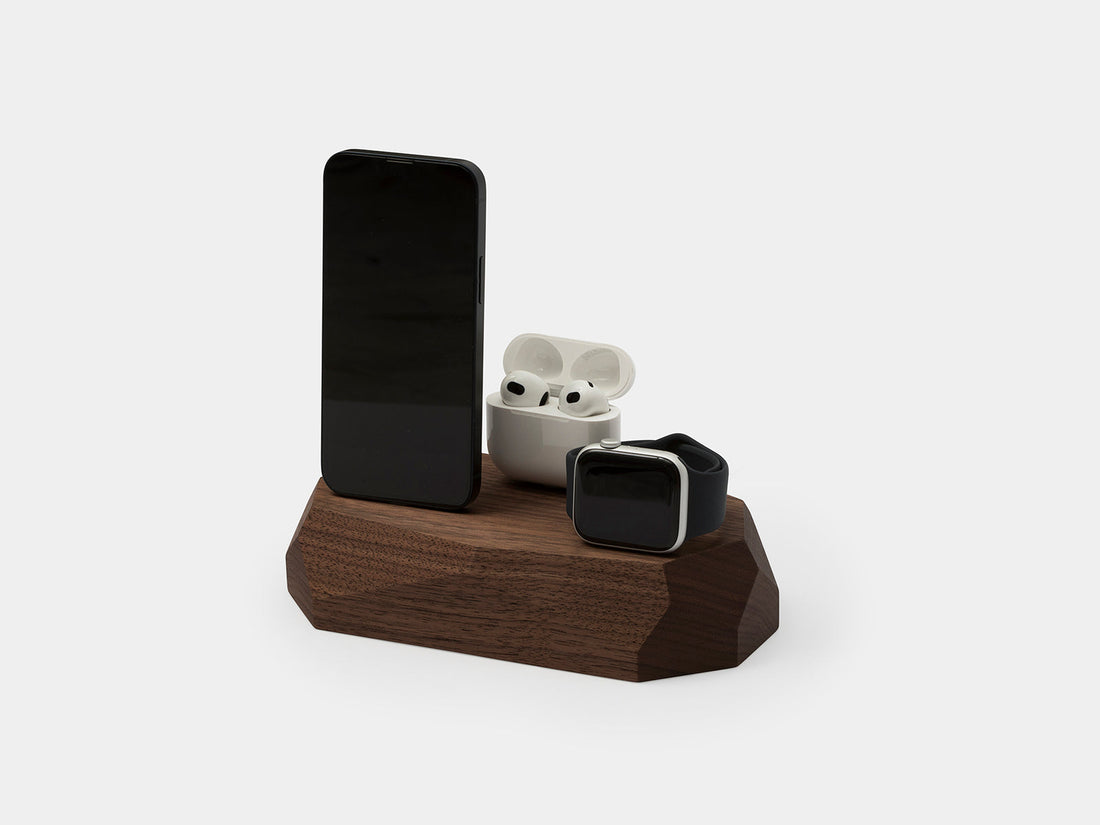 Walnut faceted dock holding a phone, an earbuds case and a watch
