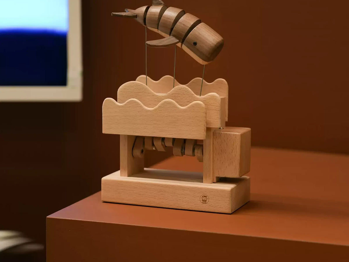 The whale automaton on a dark wood table, a screen glowing behind.