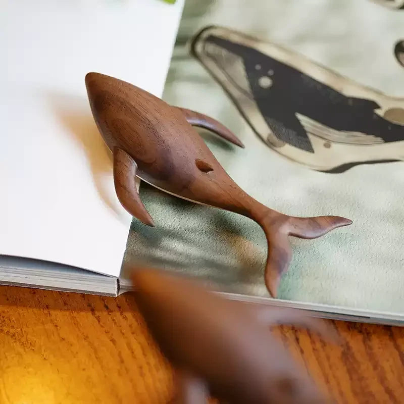 Close view of the carved walnut whale, its fins and tail, above an open sketchbook.