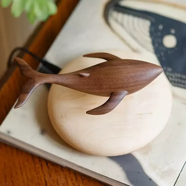Carved walnut whale floating just above a round pale maple base, a whale print on paper behind.